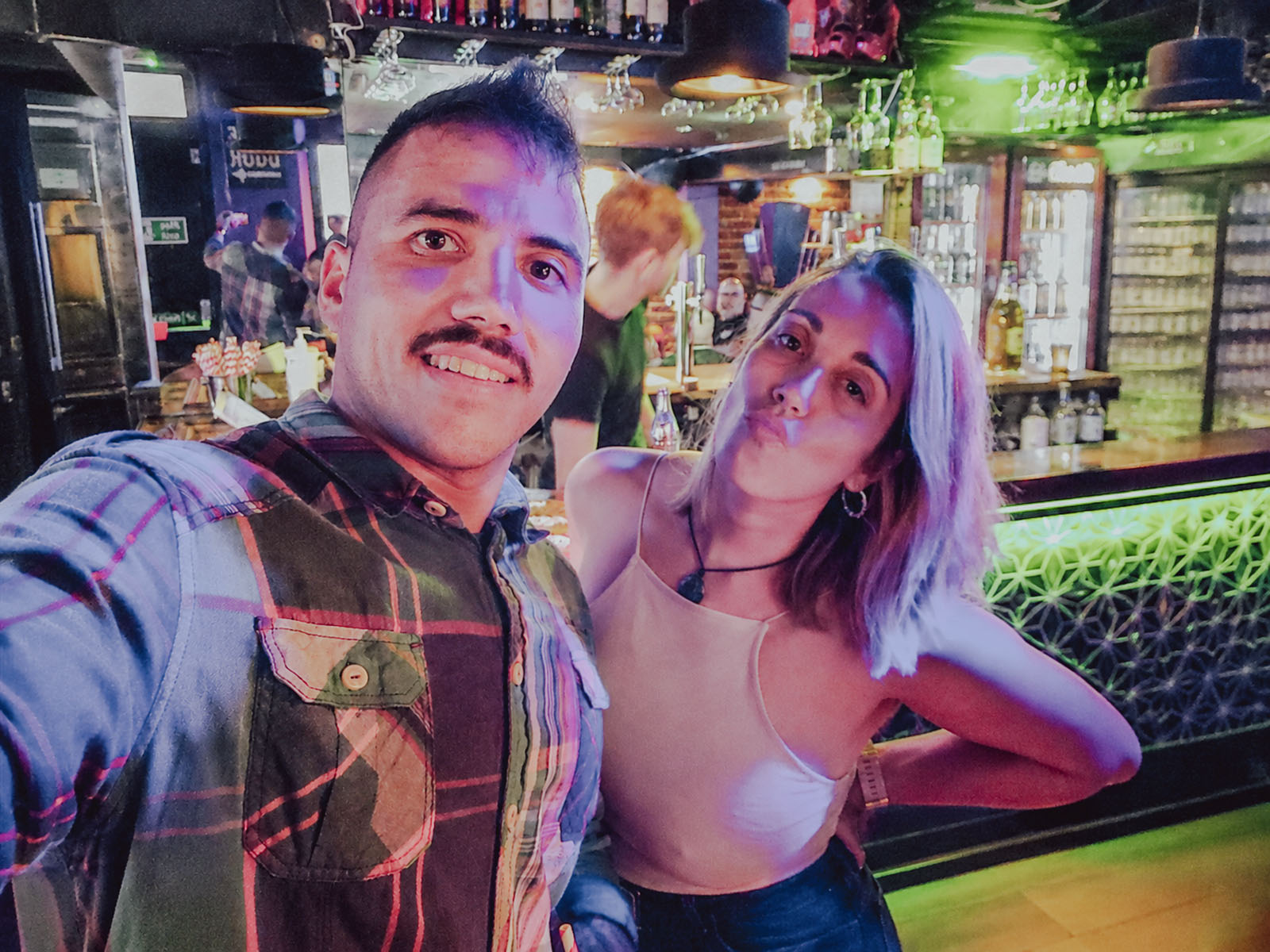 Hugo y Celia haciéndose una foto en un bar iluminado con luces de colores